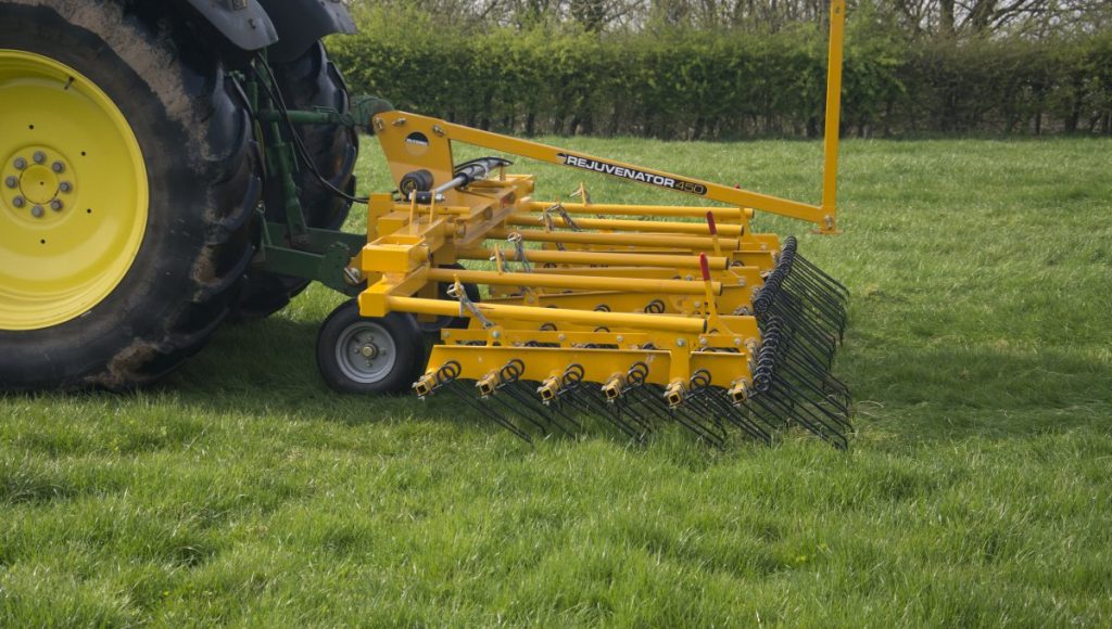 yellow spring tine harrow attached to back of tractor