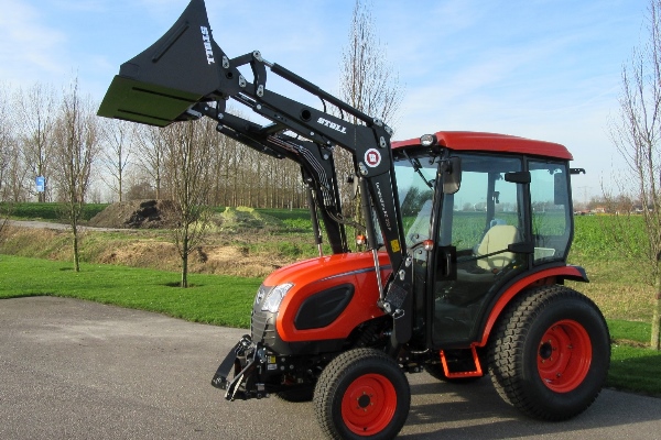 orange kioti tractor with loader and bucket raised on field background